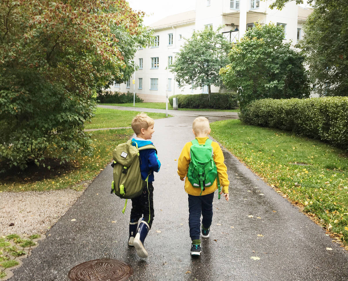 Två små skolpojkar går glada hem i sommarregnet.