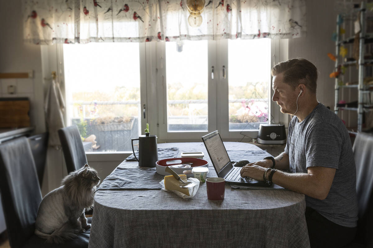 Hemarbetande man sitter med en laptop vid frukostbordet tillsammans med sin katt.