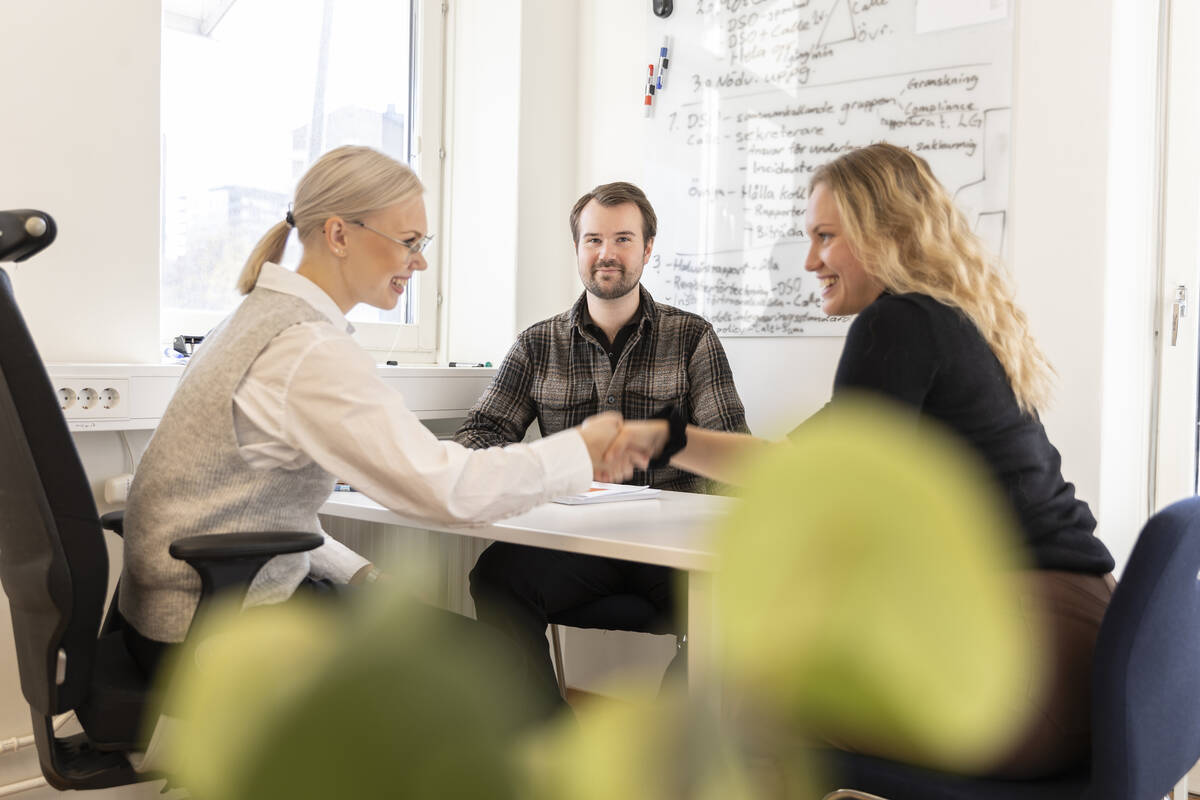Tre glada personer kommer överens inne i ett kontorsrum.