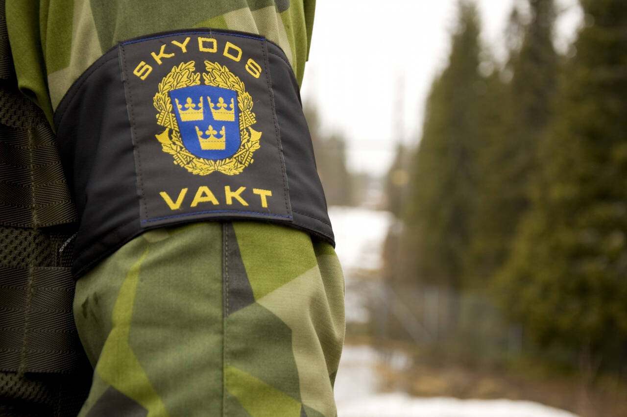 Bild på arm iklädd militärens uniform och armlapp med ordet "skyddsvakt"