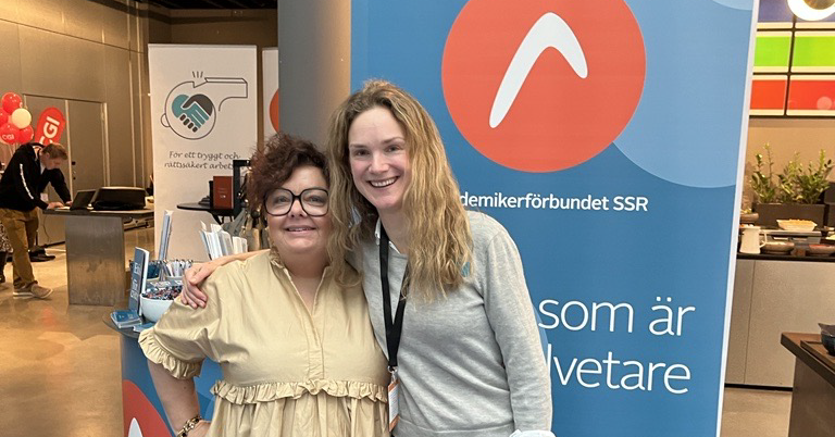 Två kvinnor framför akademikerförbundet SSR logga