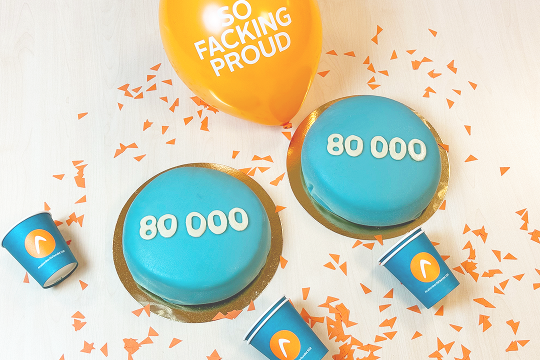 Två blåa tårtor med texten 80000 omgivna av konfetti och ballonger