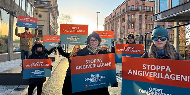 Flera personer står utanför riksdagen med plakat där det står stoppa angiverilagen