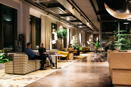 Kontorsmiljö med stora ytor och märkare jordfärger. Två personer sitter i en soffa i fonden.